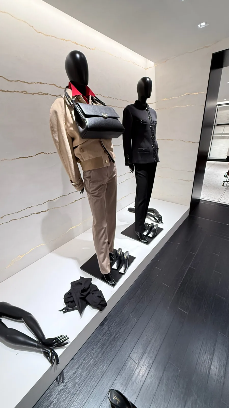 Chanel in-store window with two black mannequins against a gold-veined wall
